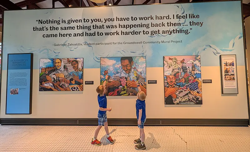 Clint and Finn viewing an exhibit about hard work at Ellis Island